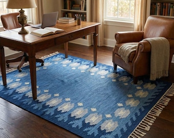 May include: A blue area rug with a floral pattern in white and light blue. The rug is rectangular with a fringed edge. The rug is in a room with a desk, chair, and bookshelves.