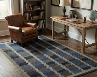 May include: A rectangular area rug with a geometric pattern in shades of blue, brown, and gray. The rug is placed on a hardwood floor, with a leather armchair and wooden desk in the background.