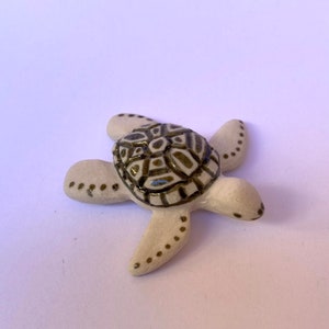 May include: A ceramic turtle figurine with a cream-colored body and a patterned, dark brown and cream shell. The turtle's flippers are dotted with small brown spots. The figurine is a decorative item.