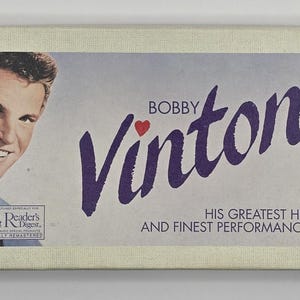 Puede incluir: Una portada de álbum vintage de Bobby Vinton. El álbum presenta un retrato de Bobby Vinton a la izquierda y el nombre "Bobby Vinton" en escritura púrpura grande con un corazón. También es visible el texto "His Greatest Hits and Finest Performances".