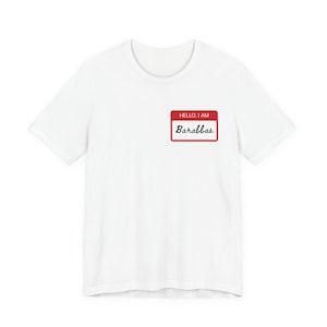 Può includere: Una maglietta bianca con un'etichetta rossa con la scritta "HELLO, I AM" sopra il nome "Barabbas" in un carattere scritto a mano. L'etichetta ha un bordo bianco.