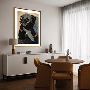 May include: A framed art print depicts a person with their face obscured by their hands. The person is adorned with gold jewelry, including rings and bracelets. The artwork is displayed in a room with a white cabinet, a round wooden table, and mustard-colored chairs.