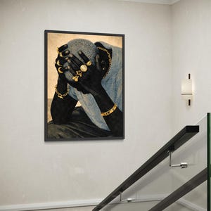 May include: Framed art print featuring a person with dark skin, wearing gold jewelry, including rings, bracelets, and a chain. The person is wearing a blue sweater and has their hands covering their face. The artwork is displayed on a white wall.