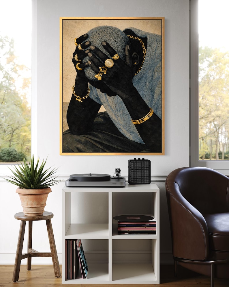 May include: A framed art print depicts a person with dark skin, wearing gold jewelry, and a light blue sweater. The artwork is displayed above a white cube shelf with a record player, speaker, and potted plant.