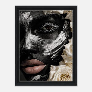 May include: Black framed art print showing a close-up of a face with black skin and white brushstrokes. The lips are a nude colour, and white roses are in the background. The art print is a portrait.