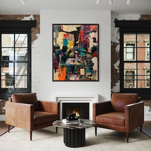 May include: A framed rectangular wall art piece featuring a vibrant, multi-colored mixed media illustration of several figures gathered around a table, displayed above a fireplace between two brown leather armchairs and a round coffee table.