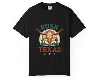May include: Black t-shirt featuring a graphic design with the text "RUSK TEXAS" above a steer skull, cactus, and sunset design. The design is in shades of brown, orange, green, and blue.