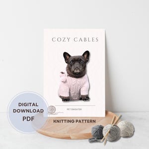 May include: A digital PDF knitting pattern titled "Cozy Cables" featuring a French Bulldog wearing a pink cable-knit sweater. The image includes text that says "Digital Download PDF" and "Knitting Pattern". Yarn and knitting needles are also visible.