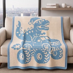 Può includere: Una coperta rettangolare all'uncinetto con uno schema di colori azzurro e crema. Il design mostra un grande dinosauro che indossa un cappello da Babbo Natale mentre guida un monster truck con pneumatici sovradimensionati, con bordo azzurro.
