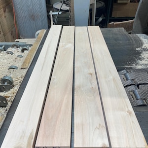 May include: Four unfinished wooden planks, each with a light, natural wood grain. The planks are labeled with dimensions and measurements in inches. The wood appears to be freshly cut and ready for use in a woodworking project.