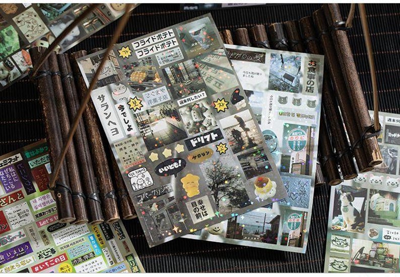 Op de afbeelding: Vellen decoratieve stickers met Japanse tekst en afbeeldingen, waaronder eten, landschappen en stripfiguren. De stickers zijn gerangschikt op een donkere ondergrond met bamboe accenten.