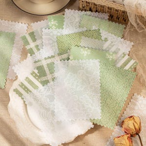 May include: A collection of rectangular fabric swatches featuring various shades of green and white. The patterns include white floral lace, green and white herringbone, plaid, and botanical prints with pinked edges, layered on a white plate.
