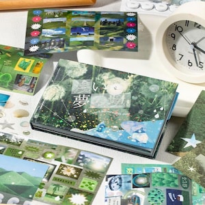 May include: A collection of decorative stickers and a small book with Japanese text and a dreamy aesthetic. The stickers feature landscape scenes, flowers, and other nature-inspired designs. A white analog clock is also visible.