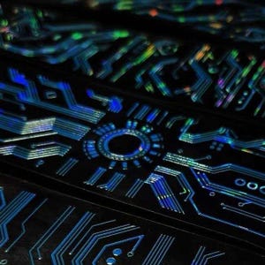 May include: A black surface featuring a holographic circuit board pattern with interconnected lines and a central circular node. The design displays iridescent blue, green, and silver light reflections across the geometric pathways.