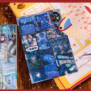 May include: A collection of decorative stickers with various designs, including blue cityscapes, Japanese text, and a calendar. The stickers are arranged on a wooden surface with other stationery items.
