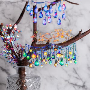 May include: A clear glass vase holds a branch with colorful leaves. Decorative stickers of light bulbs hang from branches. The light bulbs are blue, green, yellow, and orange. The background is a marble pattern.