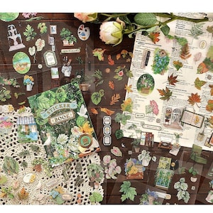 May include: A collection of decorative stickers featuring botanical and nature-themed designs. The stickers include images of plants, leaves, and small illustrations, along with a sticker book. The stickers are arranged on a wooden surface with floral accents.