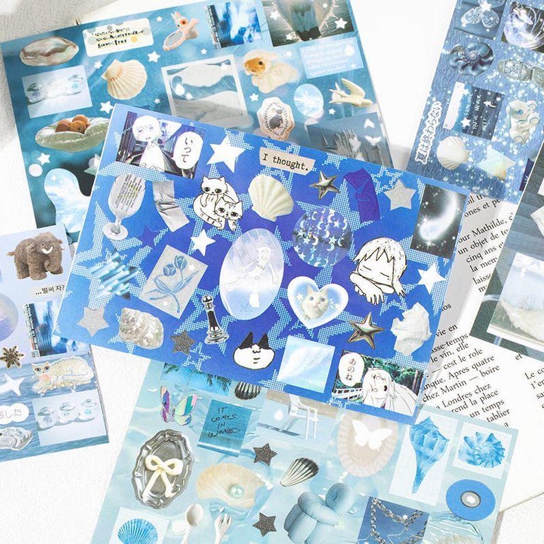 Op de afbeelding: Een verzameling blauwe en witte decoratieve stickers met diverse ontwerpen, waaronder schelpen, sterren, katten en illustraties. De stickers hebben een dromerige, grillige esthetiek met de tekst "I thought."