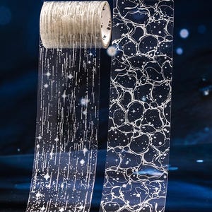 May include: Two rolls of clear adhesive tape featuring white graphic designs. One roll displays vertical lines with star-like accents, while the other roll features an organic, interconnected web pattern with small white dots and star shapes.
