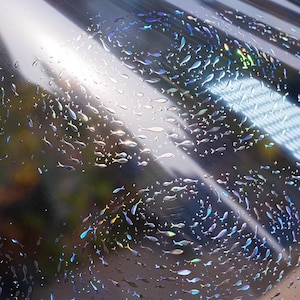 May include: Iridescent film with a pattern of small fish in various colors, including blue, green, and yellow. The fish are arranged in a swirling pattern across the surface, creating a shimmering effect. The film has a reflective, glossy finish.