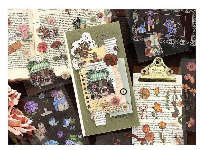May include: A collection of decorative stickers featuring floral and botanical designs. The stickers include images of flowers, storefronts, and vintage-style elements, arranged on a notebook and clipboard.