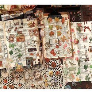 May include: An open book with vintage-style stickers and embellishments. The stickers include leaves, flowers, bows, and small illustrations. The background is a printed page with text. A white crocheted doily is in the foreground.