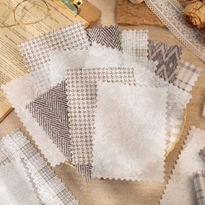 May include: A collection of fabric swatches in various patterns and textures. The swatches include white lace, herringbone, and houndstooth designs in neutral tones. The fabrics are arranged on a neutral surface, suggesting a craft or design theme.
