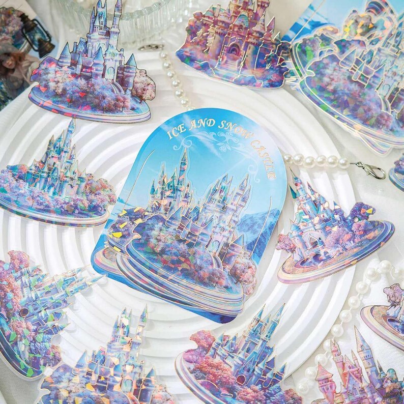 Op de afbeelding: Een verzameling iriserende stickers met fantasiekastelen in blauwe, paarse en roze tinten. De stickers hebben een holografisch effect en de tekst "Ice and Snow Castle". De stickers zijn gerangschikt op een wit oppervlak.