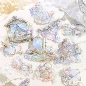 May include: A collection of iridescent stickers featuring a light blue and white color scheme. The stickers depict various objects, including a gazebo, a vanity, a dress, a pocket watch, and an envelope, all adorned with floral accents and a vintage aesthetic.