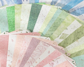 May include: A collection of decorative paper sheets in various colors, including shades of green, pink, and white. The paper has textured surfaces and decorative patterns, with some sheets featuring floral designs. The sheets are arranged in a fan shape.