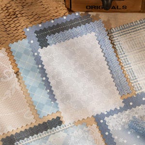 May include: Assortment of fabric swatches in various shades of blue, gray, and white. Patterns include polka dots, lace, and herringbone. The edges are cut with a zig-zag pattern. The word "ORIGINALS" is visible on a wooden box in the background.