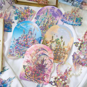 Op de afbeelding: Een verzameling kleurrijke stickers en versieringen met fantasiethema's. De stickers tonen ingewikkelde kasteelontwerpen met iriserende en glinsterende details. Sommige stickers hebben tekst zoals "Ice and Snow Castle" en "Castle Pink Illusion".