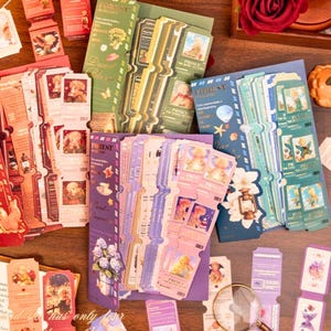 May include: A collection of vintage-style paper ephemera, including bookmarks and tags, in various colors such as red, green, blue, and purple. The designs feature illustrations of children, flowers, and text. Some items have a ticket-like shape.