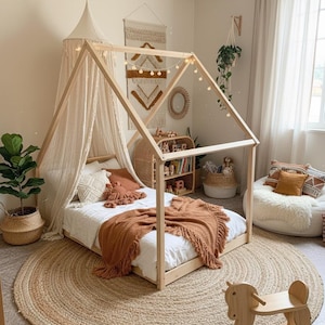 Puede incluir: Un dormitorio infantil acogedor con una cama con estructura de casa de madera, adornada con un dosel color crema y una manta color óxido. Una alfombra redonda de yute se encuentra debajo de la cama, y un caballito balancín de madera está en primer plano.