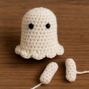 Puede incluir: Un fantasma de ganchillo hecho a mano, de color blanco roto, con ojos negros y un borde inferior festoneado. Tambi&eacute;n hay dos piezas de ganchillo separadas y a juego con colas de hilo blanco. El fantasma est&aacute; sobre una superficie de madera.
