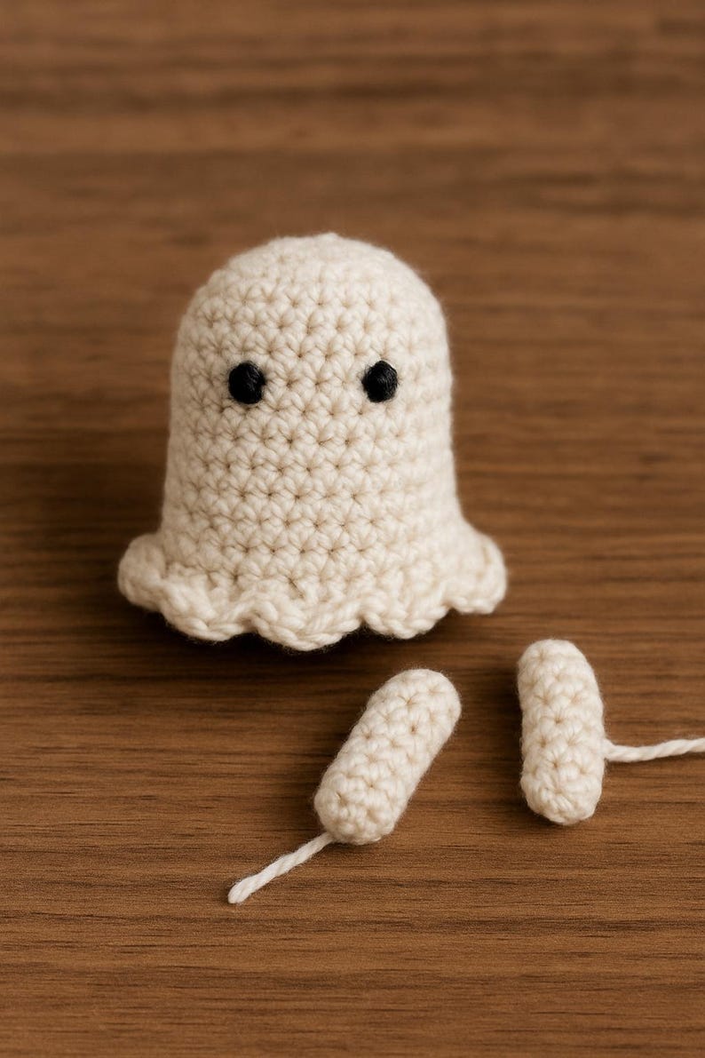 Puede incluir: Un fantasma de ganchillo hecho a mano, de color blanco roto, con ojos negros y un borde inferior festoneado. Tambi&eacute;n hay dos piezas de ganchillo separadas y a juego con colas de hilo blanco. El fantasma est&aacute; sobre una superficie de madera.