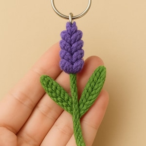 May include: A handmade lavender flower keyring. The flower is crocheted with a purple bloom and green stem and leaves. The keyring is attached to a silver-coloured metal ring.