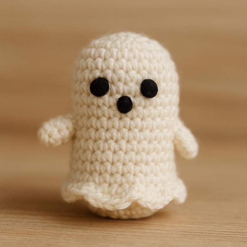 Puede incluir: Un peque&ntilde;o fantasma de ganchillo hecho a mano, en hilo blanco roto. El fantasma tiene dos ojos negros de bot&oacute;n y una boca negra. Tiene brazos peque&ntilde;os y un borde inferior festoneado. El fondo es una superficie marr&oacute;n claro borrosa.