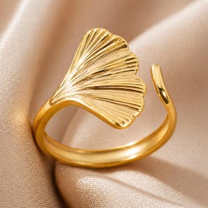Peut inclure: Une bague dorée ornée d'une feuille de ginkgo. La bague est de conception ouverte, permettant de légers ajustements de taille. Le détail de la feuille est finement travaillé avec des nervures visibles, ajoutant de la texture et de l'intérêt visuel au bijou.