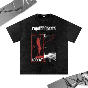 Puede incluir: Camiseta negra con lavado vintage con las palabras "rigatoni pasta" sobre un gráfico rojo y blanco. El gráfico presenta una silueta y el nombre "ROBERT" en rojo.