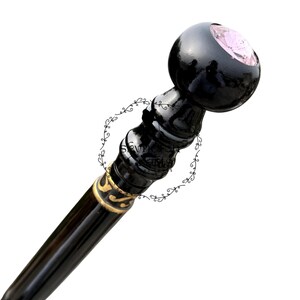 Può includere: Bastone da passeggio nero con finitura lucida. L'impugnatura è una sfera arrotondata con un'incastonatura di pietra preziosa rosa. L'asta ha dettagli dorati e un design decorativo. Il bastone è progettato per supporto e stile.