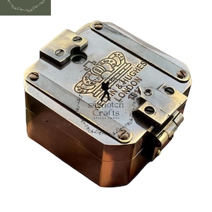 Può includere: Una bussola in ottone di forma quadrata, con l'iscrizione "John & Hughes London 1917" e un'emblema a corona. La bussola ha viti a vista e un coperchio incernierato. L'articolo è di "Skynotch Crafts".