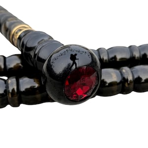 Könnte beinhalten: Schwarzer Wanderstock mit dekorativem Griff mit rotem Edelstein und Wanderer-Silhouette. Der Stock hat eine glänzende Oberfläche mit goldenen Akzenten. Der Griff hat ein detailliertes Design mit einer Wanderer-Silhouette und dekorativen Schnörkeln.