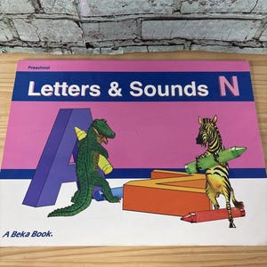 May include: A preschool educational book titled Letters & Sounds N by A Beka Book. The cover features a pink and blue background with a large purple letter A, an orange letter N, a green alligator holding a yellow crayon, and a zebra holding a green crayon.