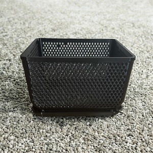 May include: A dark brown, square metal basket with a diamond-patterned mesh design. The basket has a solid base and a perforated top edge. The basket is sitting on a bed of small, light-colored pebbles.