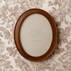 Puede incluir: Un marco ovalado de madera con el texto "But as for me and my house, we will serve the Lord. - Joshua 24:15." El marco es de color marrón oscuro, y el fondo es un estampado floral en tonos marrones y crema.
