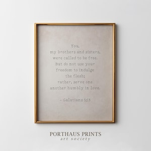 Puede incluir: Una impresión enmarcada con un marco dorado. La impresión presenta una cita de Gálatas 5:13 en una fuente simple y elegante. El fondo es de color beige neutro. Las palabras "PORTHAUS PRINTS art society" están en la parte inferior.