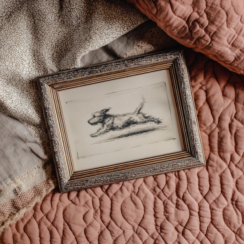 May include: A framed pencil sketch of a dog in mid-leap. The artwork is in a gold-colored frame with a detailed border. The dog is depicted in motion, with its legs extended. The background is a neutral color.