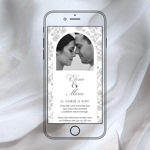 以下が含まれることがあります： スマートフォンには、白黒の結婚式の招待状が表示されています。招待状には、カップルの写真、「Elena & Marco」という名前、フランス語のテキストが記載されています。花の模様が写真を囲んでいます。