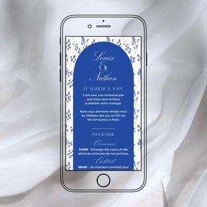 以下が含まれることがあります： スマートフォンには、デジタル結婚式の招待状が表示されています。「Louise & Nathan」という名前がイベントの詳細の上にエレガントなスクリプトで表示されています。デザインには青いアーチと花のアクセントが含まれており、フランス語で情報が記載されています。